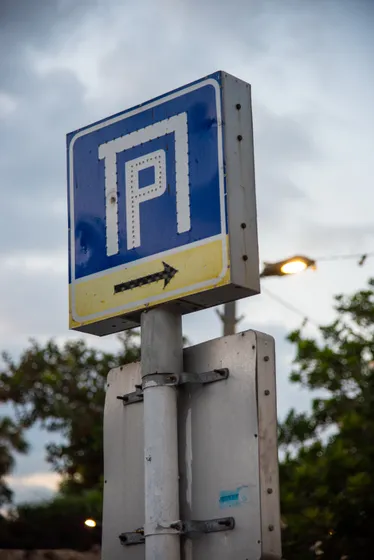 A weathered blue parking sign against an overcast sky