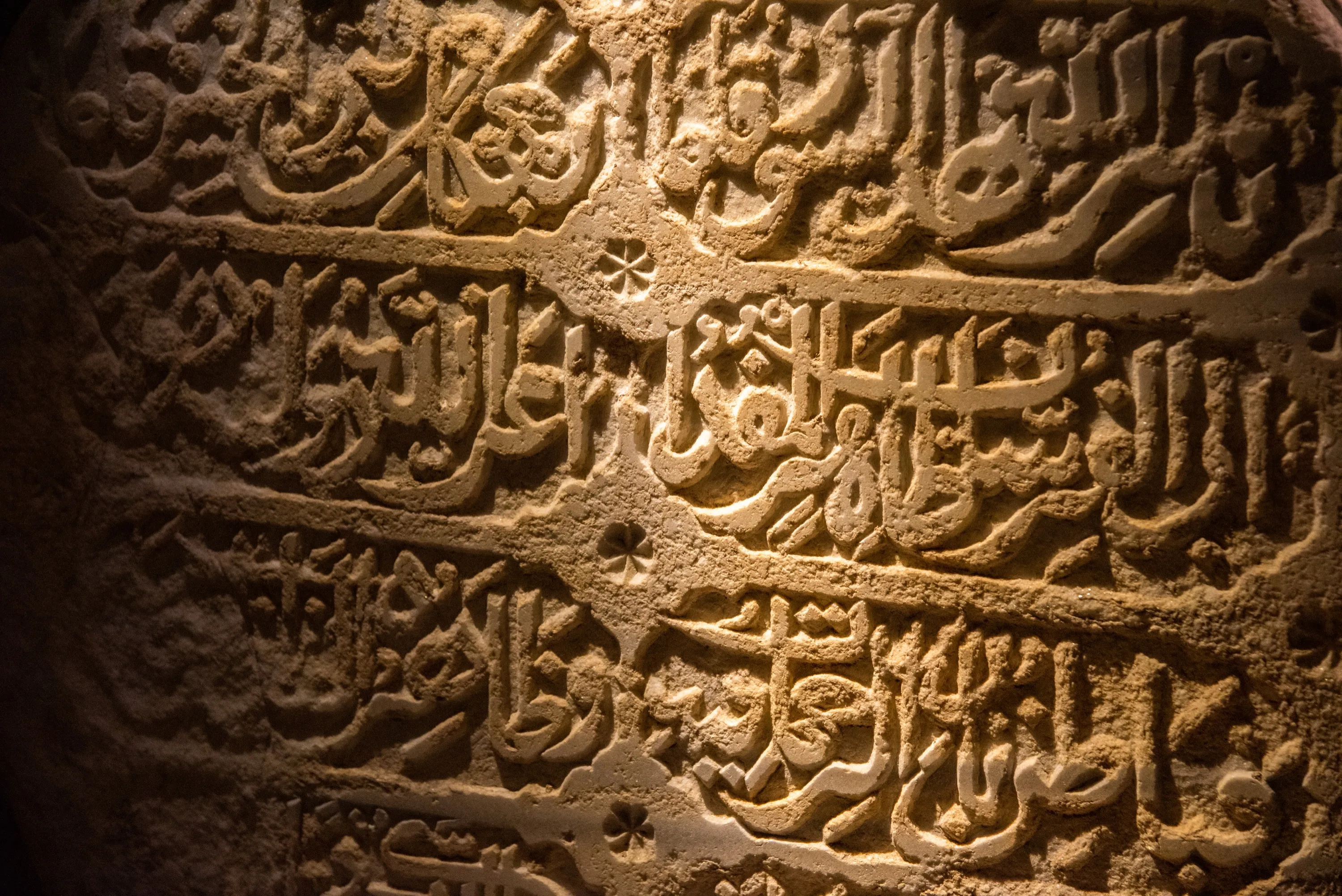 Arabic inscription carved into stone, lit from the side