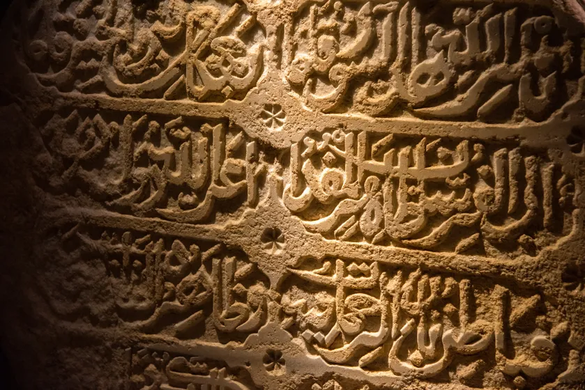 Arabic inscription carved into stone, lit from the side