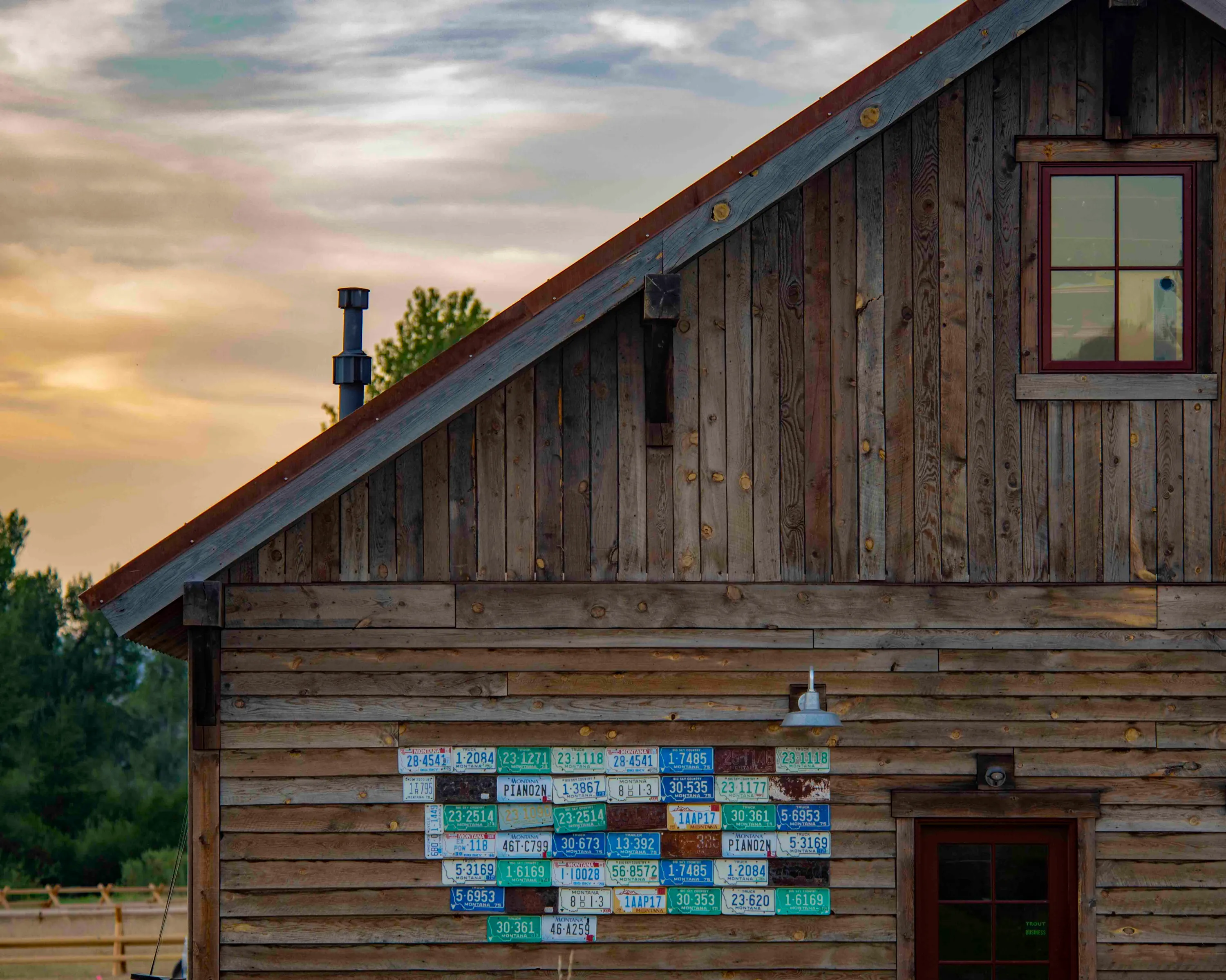 A barn wall covered in old license plates at dusk